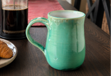 Handmade green crystalline pottery mug on dark wooden table