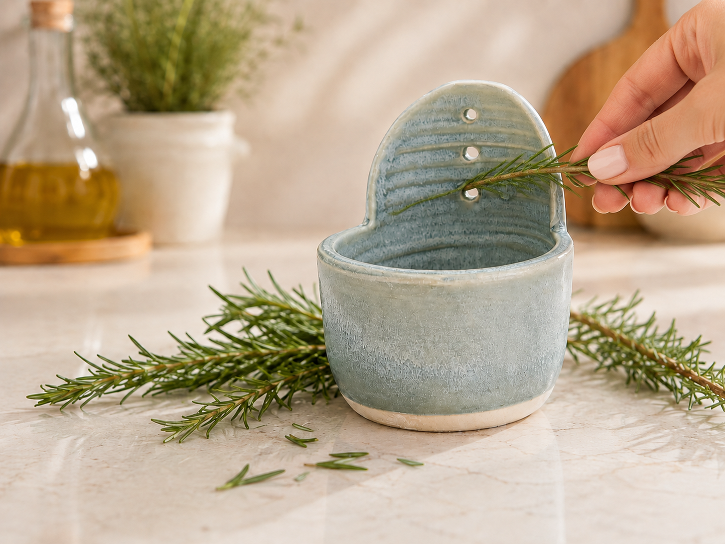 Handmade ceramic herb stripper in soft blue grey glaze with fresh rosemary being pulled through the centre hole in a kitchen setting