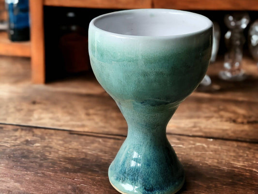 Handmade ceramic goblet with green glaze on wood table