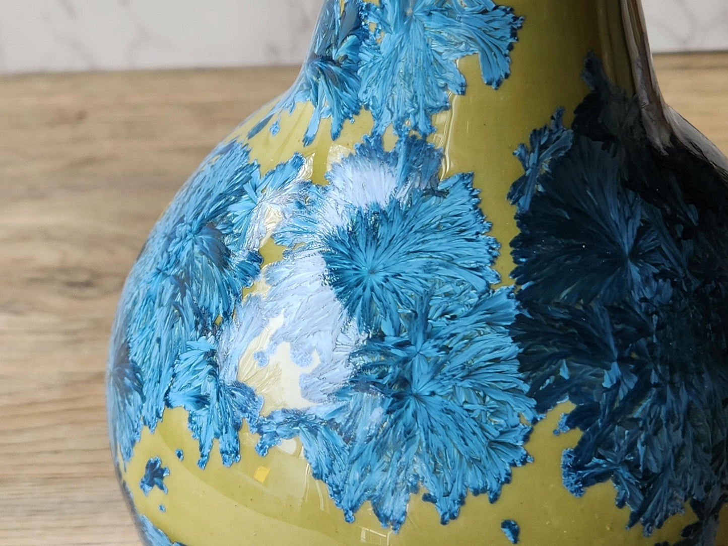 close up of feathery crystals on porcelain vase with high-gloss mustard base and blue crystals