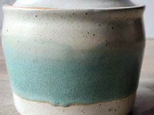 Close up of the green and speckled cream glaze on the handcrafted pottery jar.