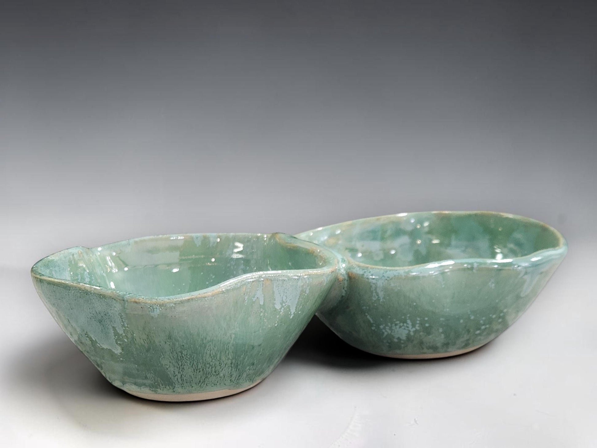 Artisan ceramic divided serving bowl handmade by Buxton Pottery, featuring two connected compartments and unique glaze variations.