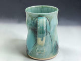 Rustic handmade stoneware mug with flowing aqua, green and dark earthy tones on grey studio sweep