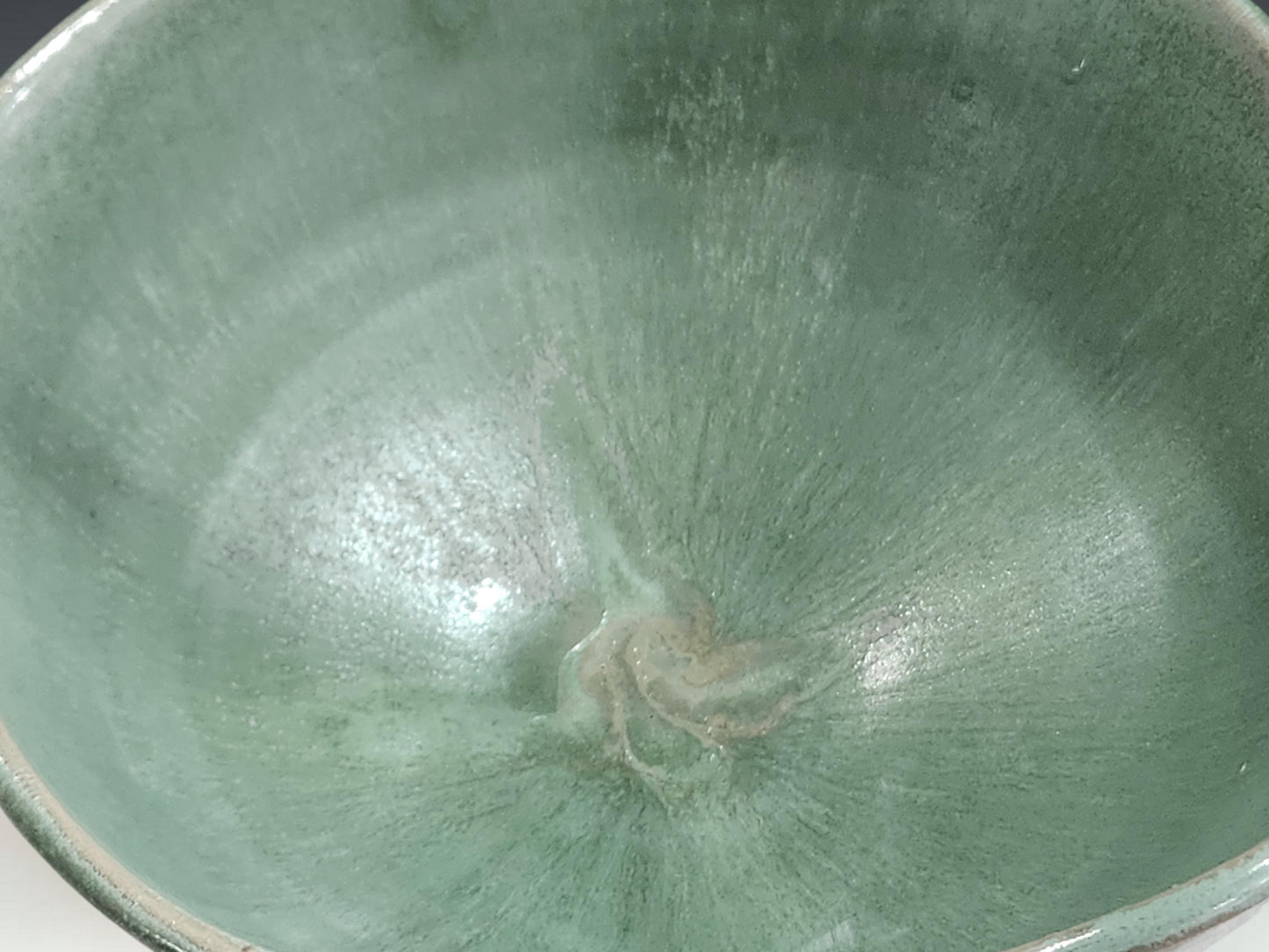 Close-up of handmade ceramic bowl showing layered seafoam green glaze and soft rim detail