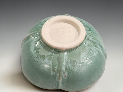 Handmade ceramic bowl on grey studio background showing altered rim, foot ring and green glaze variation