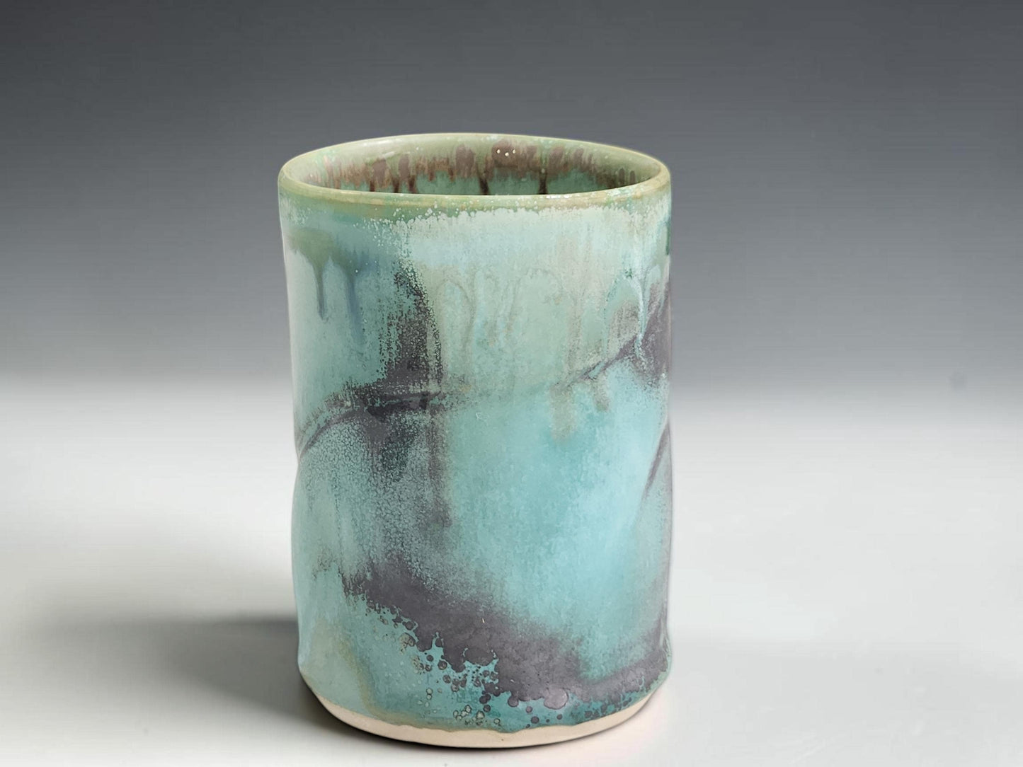 Small handmade pottery cup with straight-sided shape and organic green blue glaze variation