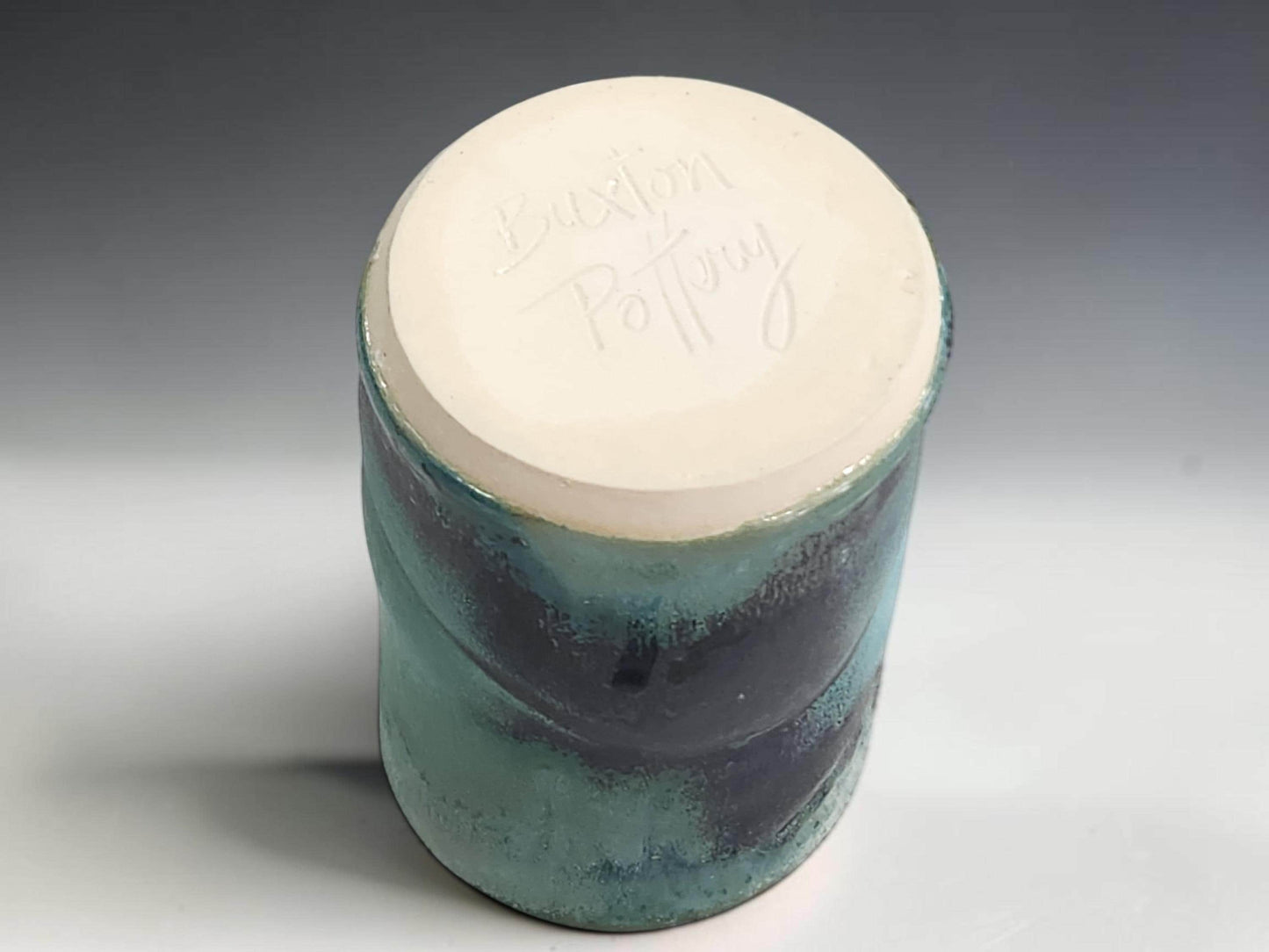 Handmade pottery tumbler on grey studio background showing compact shape and layered turquoise green glaze