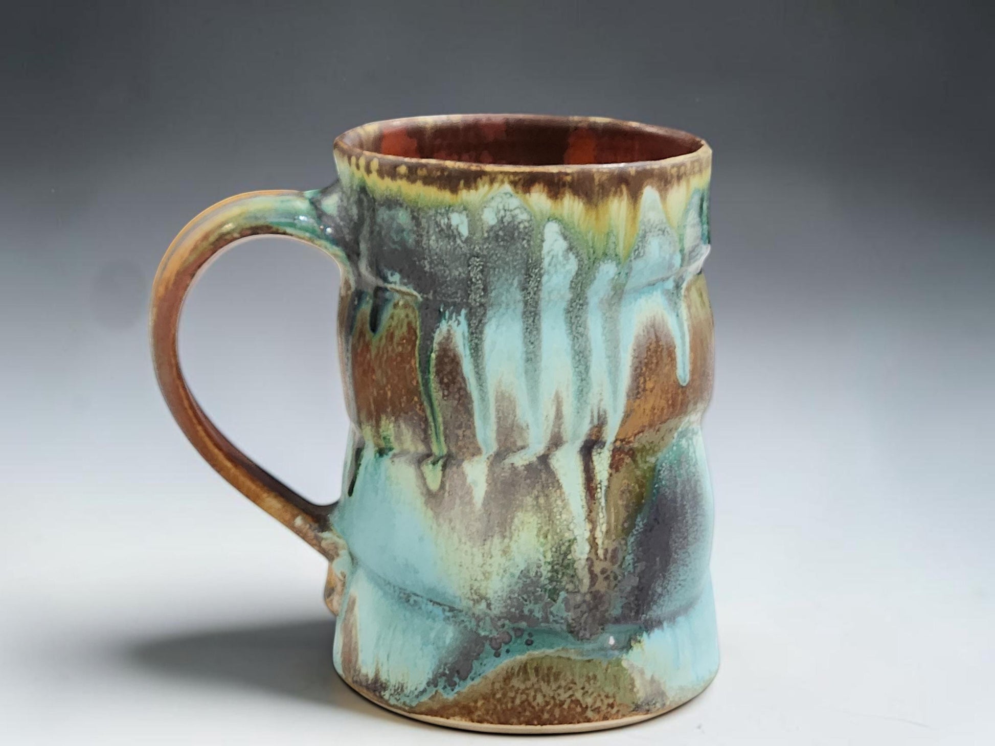 handmade ceramic mug showing turquoise, rust, brown and ash glaze drips with glossy red brown interior