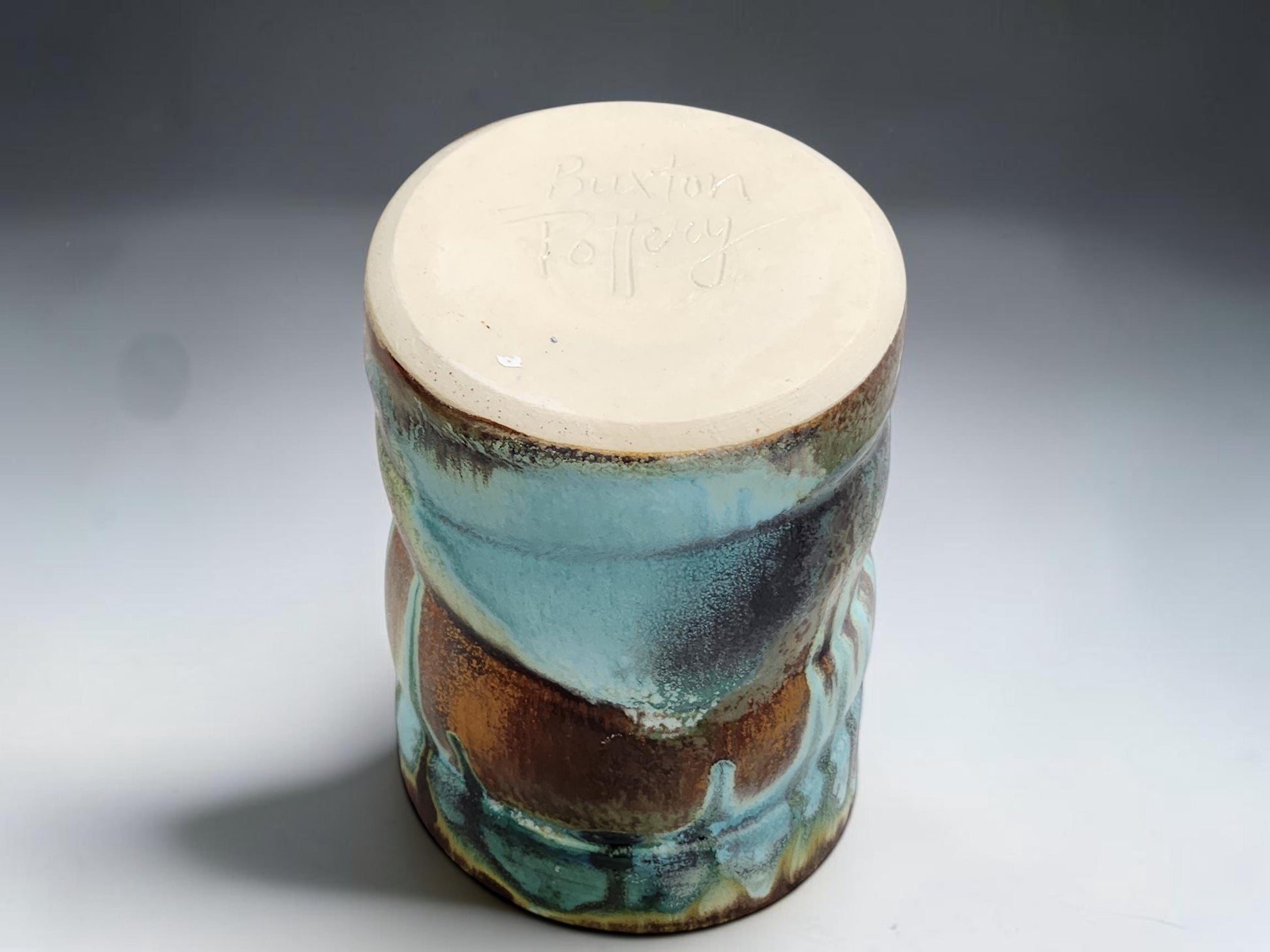 Handmade pottery mug on grey studio background showing handle, glaze movement and red brown lining