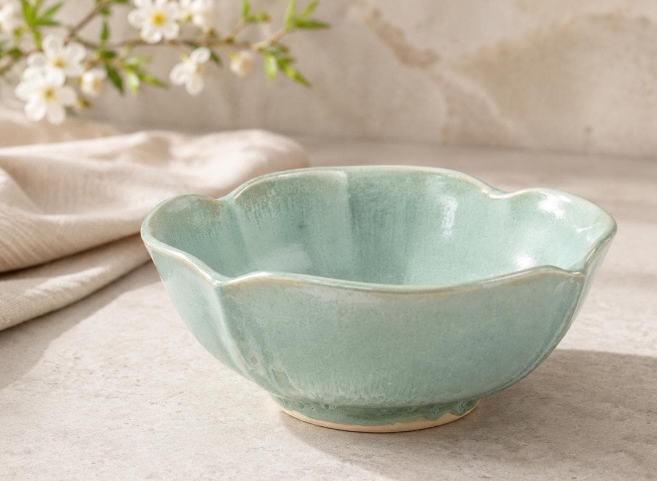 Handmade seafoam green ceramic bowl with altered petal rim styled in a warm kitchen setting
