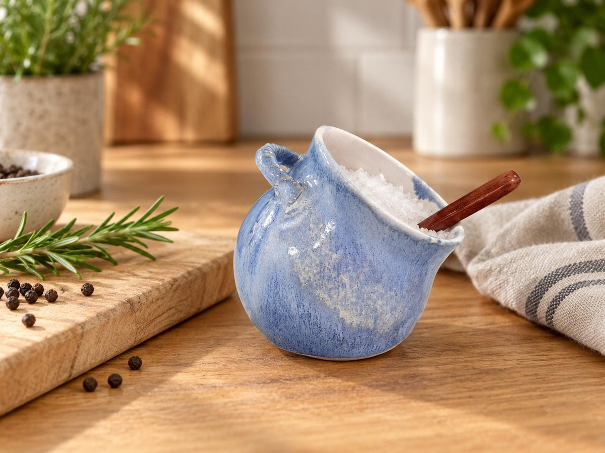 Handmade blue ceramic salt pig filled with salt on a timber kitchen bench