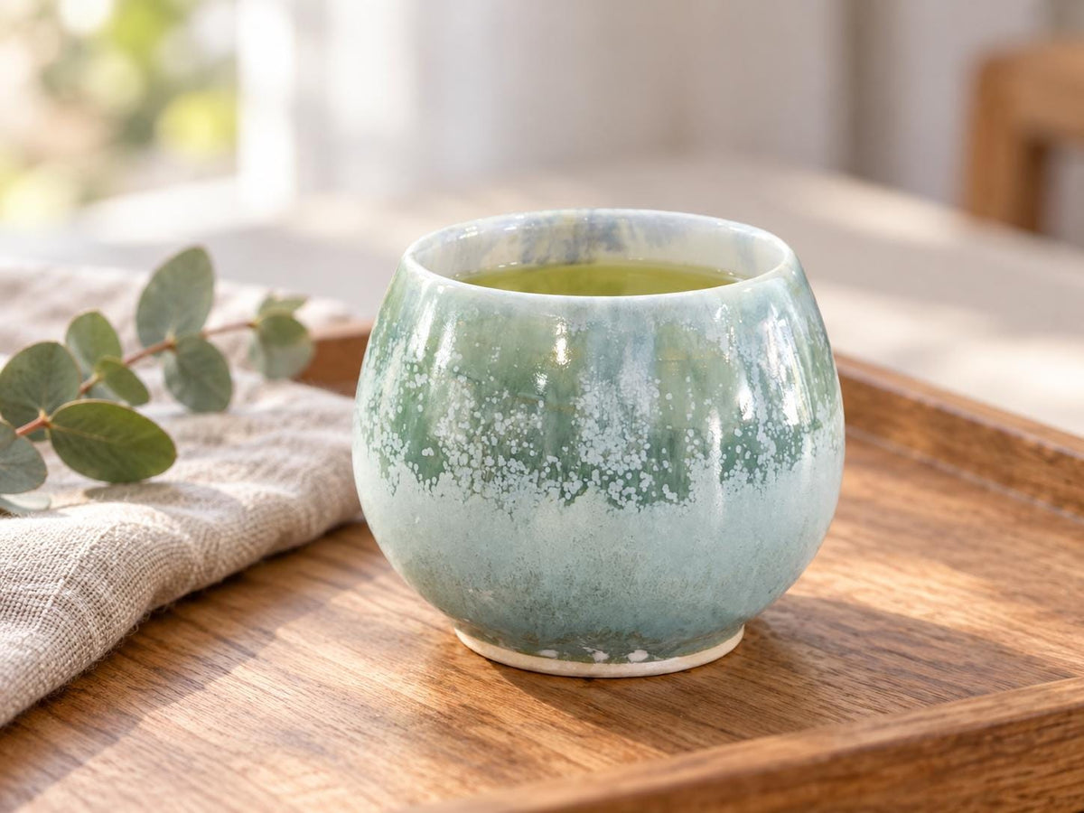 Handmade 250ml Japanese-style tea cup in soft green mottled glaze on timber tray