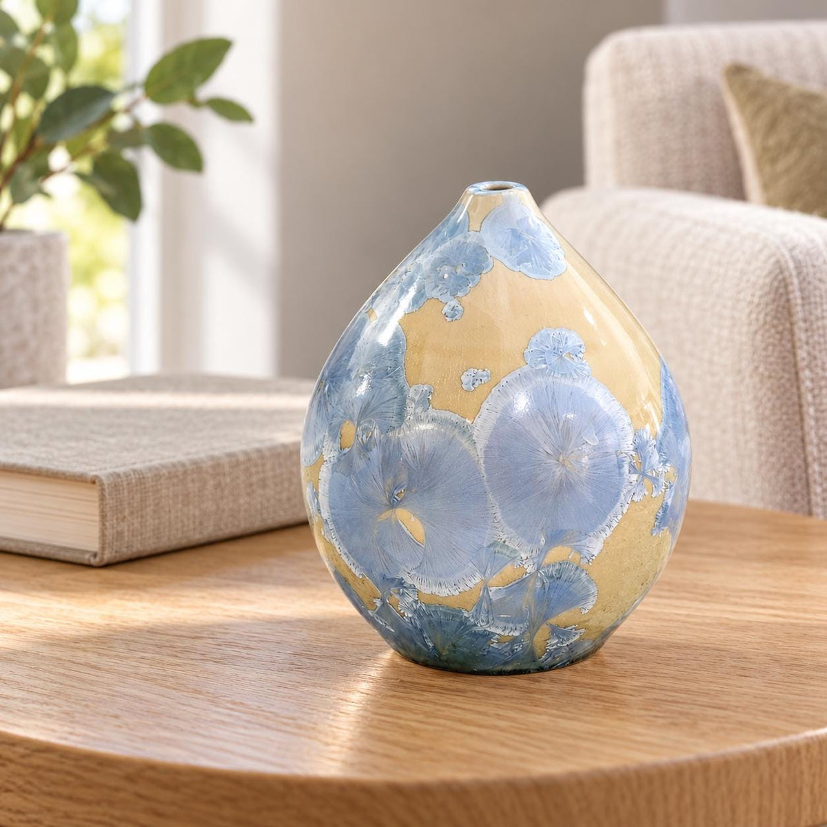 Small blue and cream crystalline pot on an oak side table beside a book in a softly lit living room.
