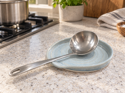 Large blue grey pottery spoon rest with stainless steel ladle in a kitchen setting