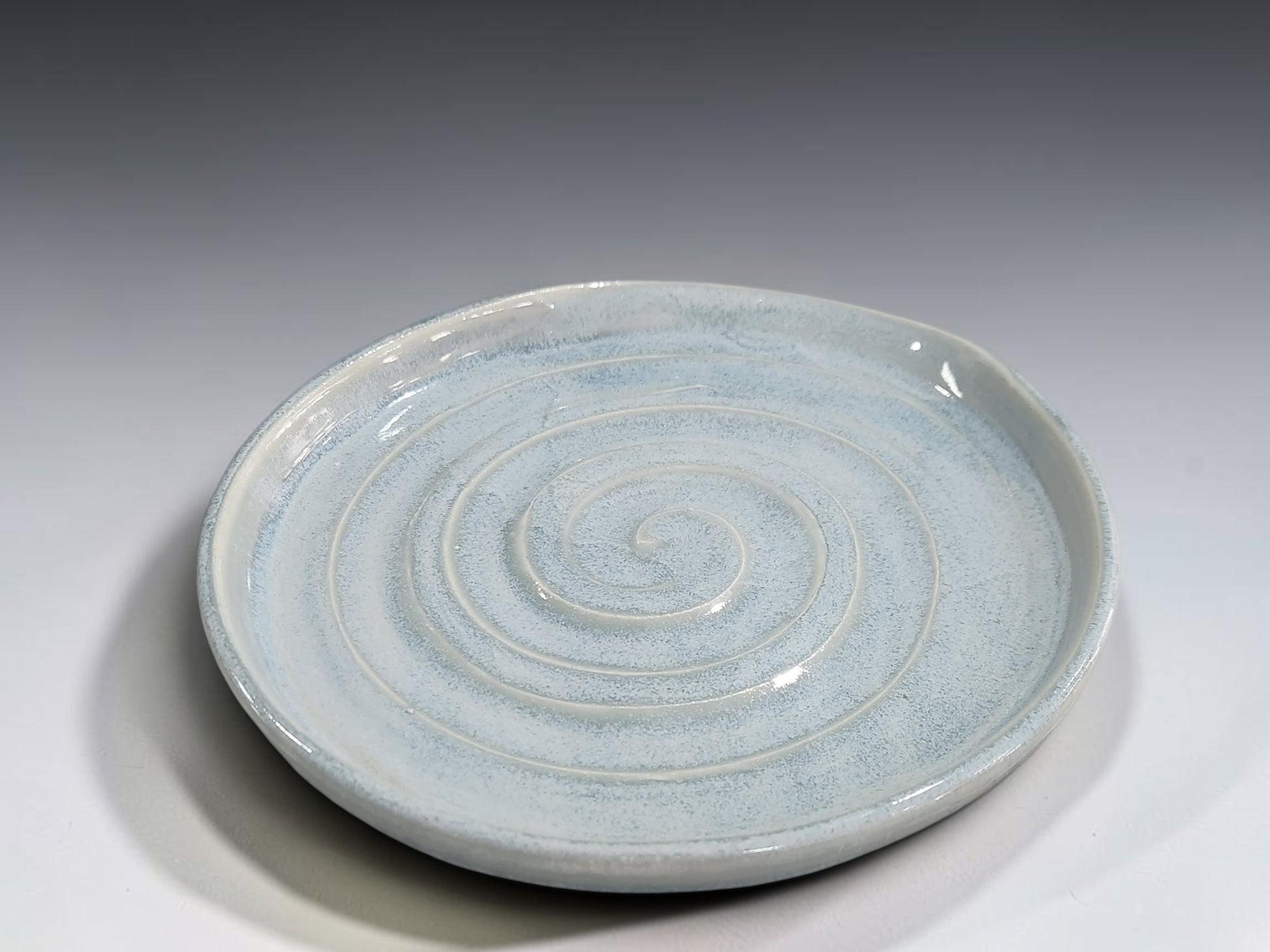 Handmade pottery utensil rest with spiral pattern and gently raised rim