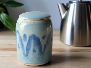 Ceramic jar with blue design on a wooden surface next to a metal teapot