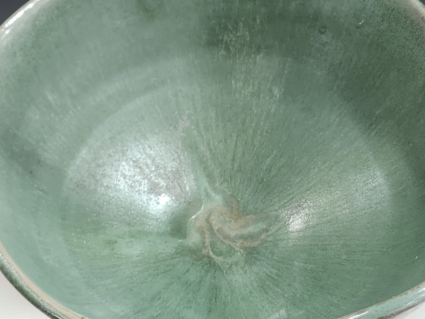 Close-up of handmade ceramic bowl showing layered seafoam green glaze and soft rim detail