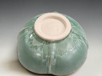 Handmade ceramic bowl on grey studio background showing altered rim, foot ring and green glaze variation