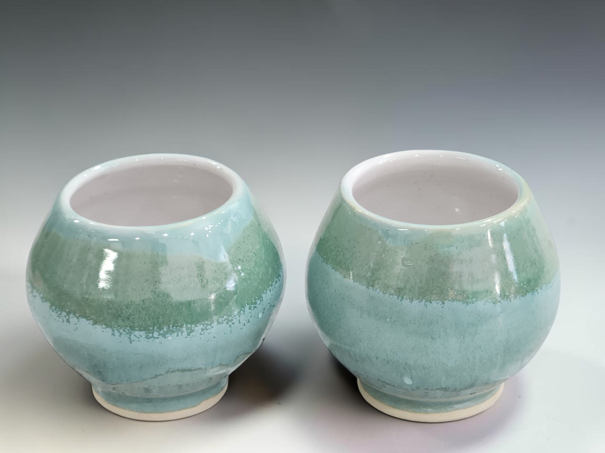 Artisan ceramic teacups with rounded form and soft mottled green glaze, handcrafted for tea lovers and collectors of handmade pottery.