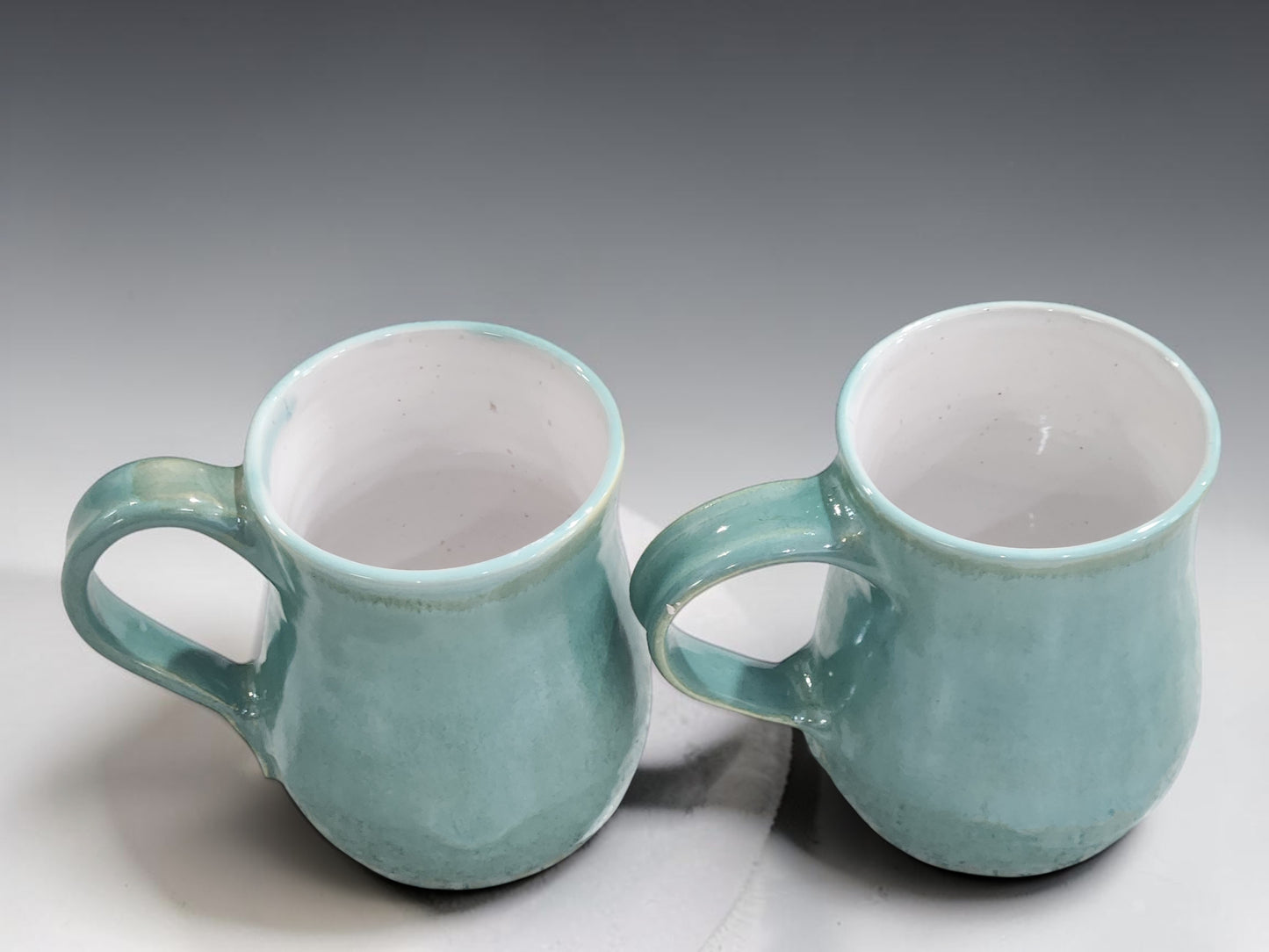 Wheel-thrown pottery mug with comfortable handle, glossy white interior and soft green glaze, handcrafted by Buxton Pottery.