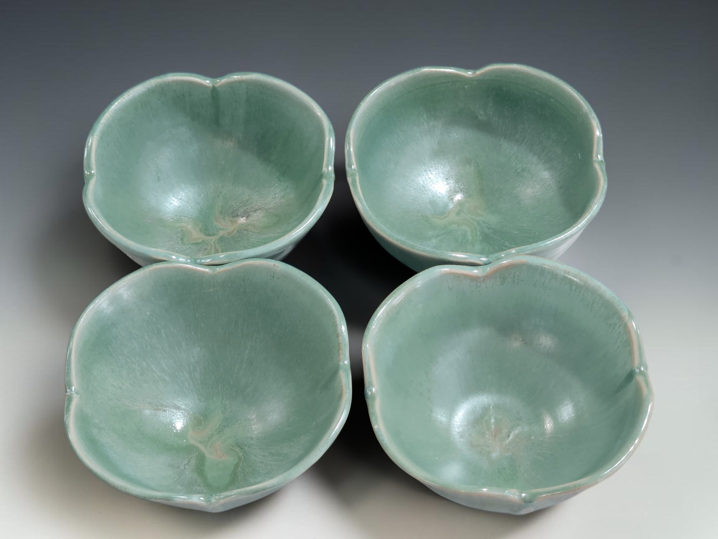 Four handmade ceramic bowls in seafoam green glaze showing small-batch variation