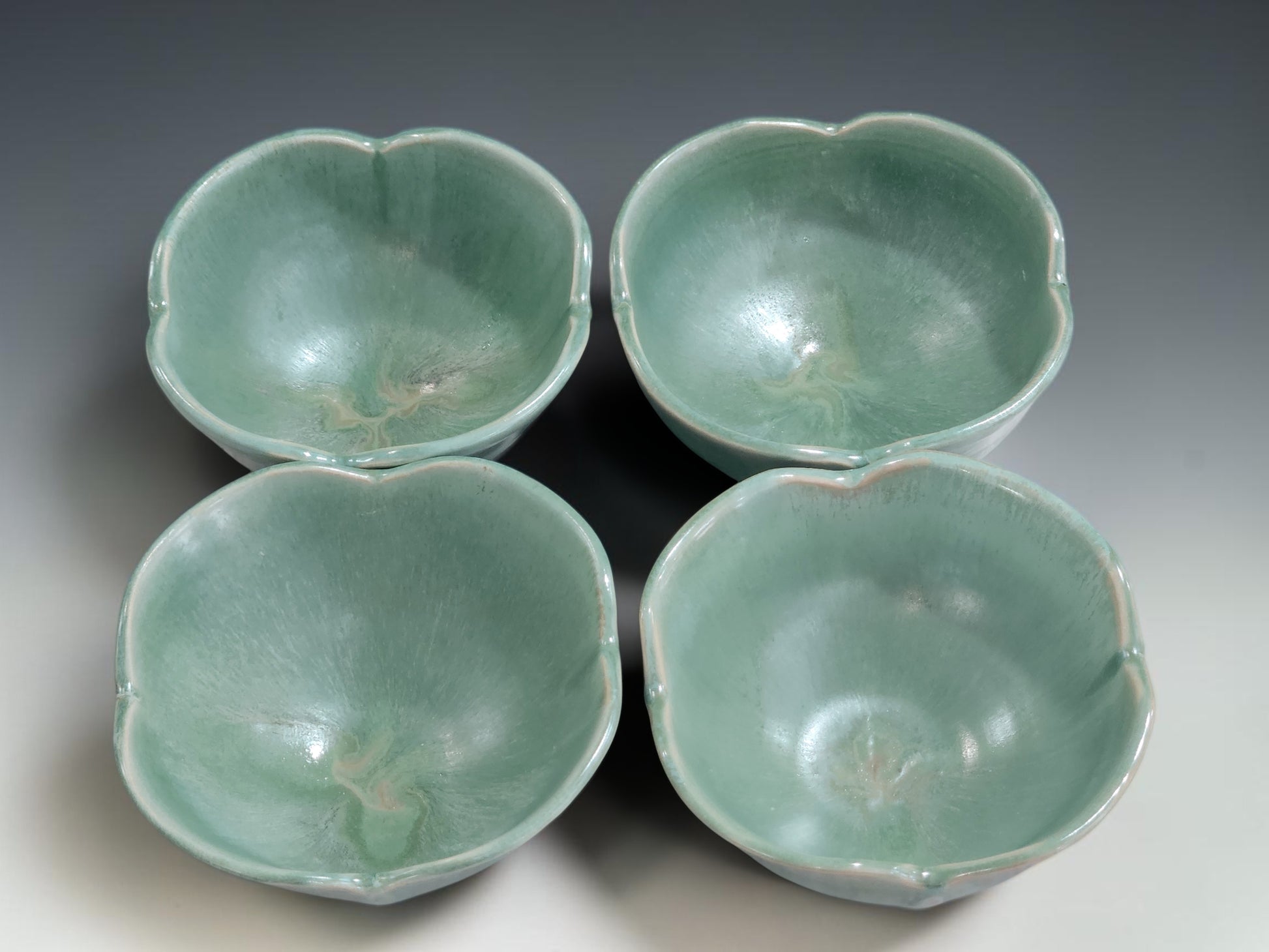Four handmade ceramic bowls in seafoam green glaze showing small-batch variation