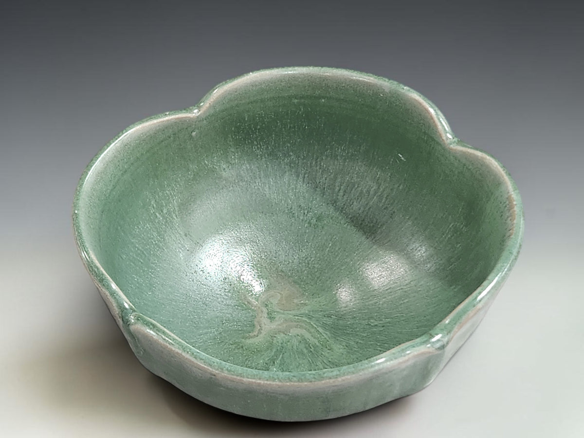 Handmade pottery bowl on grey studio background showing altered rim, foot ring and green glaze