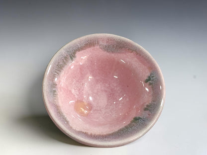 A handmade ceramic bowl with a glossy pink interior and a textured, speckled gray and white exterior, photographed on a neutral gray gradient background.