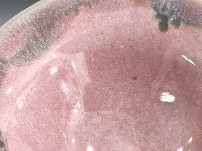 Close-up of the pink glazed interior and mottled rim of a handmade ceramic bowl.