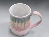 Pink pottery mug with soft green drip glaze and curved handle