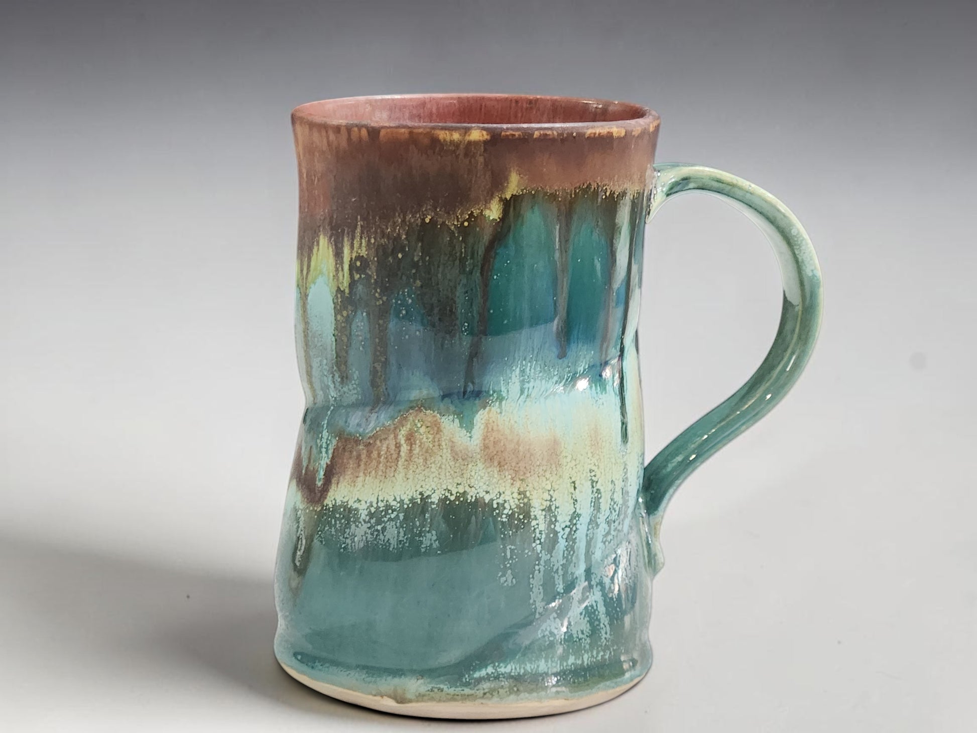 Handmade ceramic coffee mug with turquoise, amber and earthy brown flowing glaze.