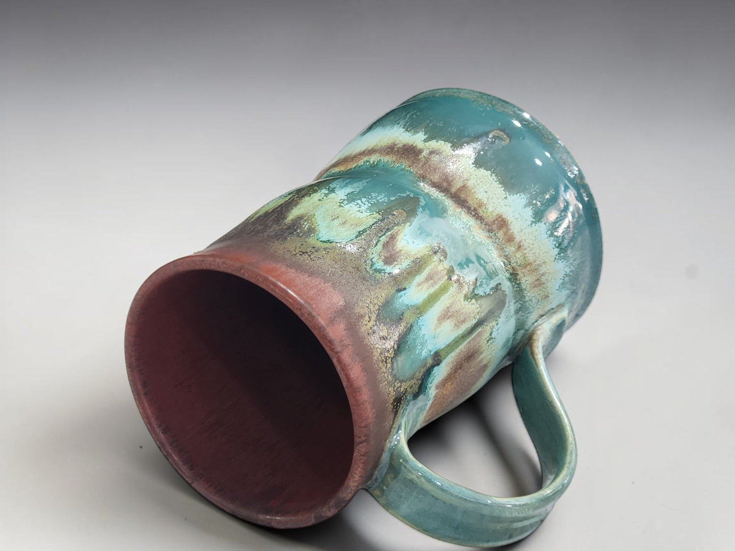Detailed close-up of the flowing turquoise and iron brown glaze on a handmade mug.