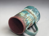 Detailed close-up of the flowing turquoise and iron brown glaze on a handmade mug.