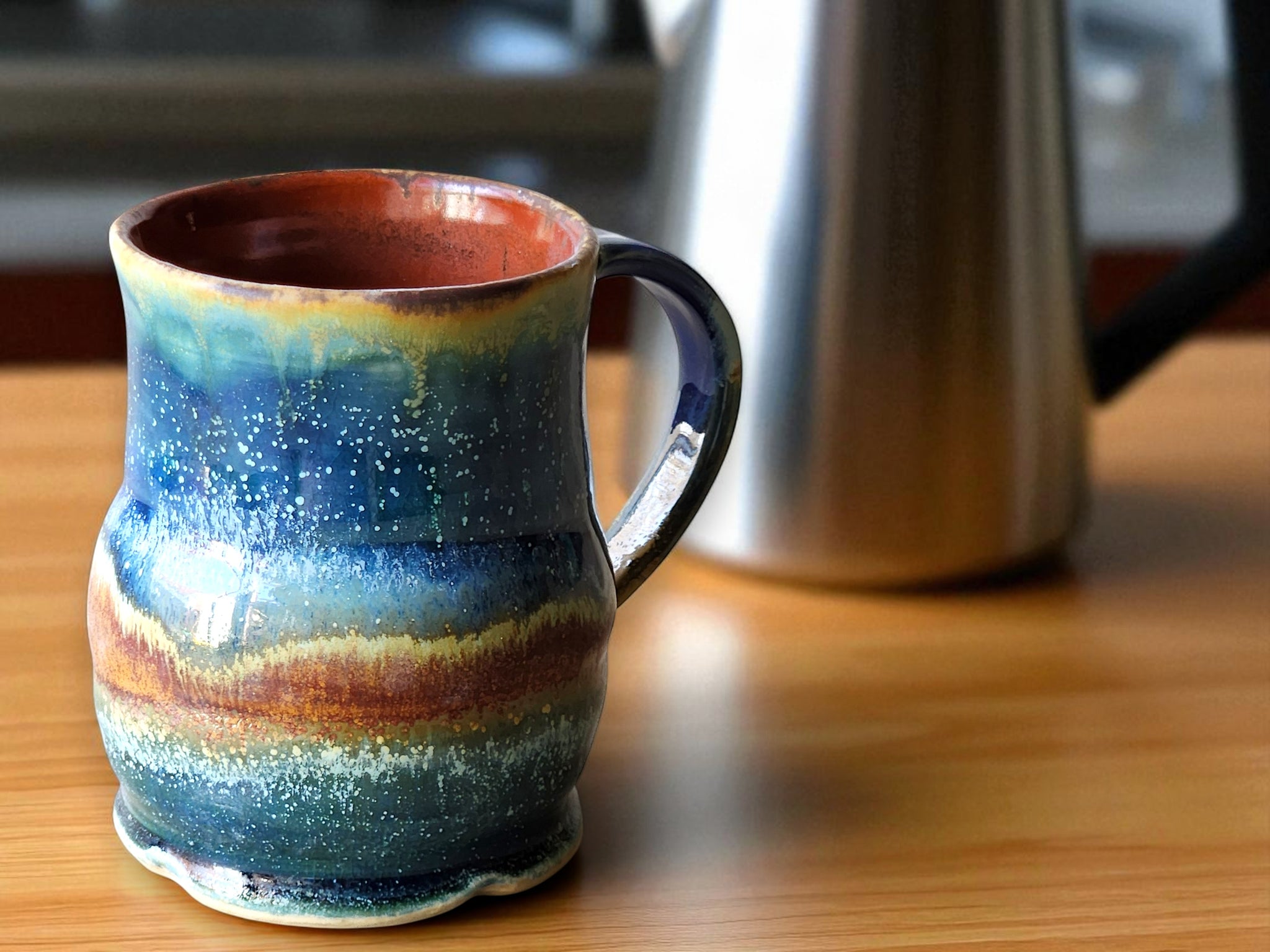 Dark green and rust red glazes intertwine on this one-of-a-kind mug. The hand-altered shape invites the 
glazes to settle in organic layers.