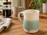 Handmade cream and green pottery mug in a lifestyle coffee setting