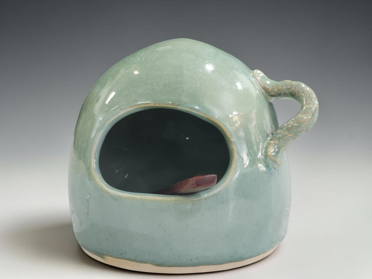 Handmade ceramic salt pig on grey studio background showing opening, rounded shape and spoon holder