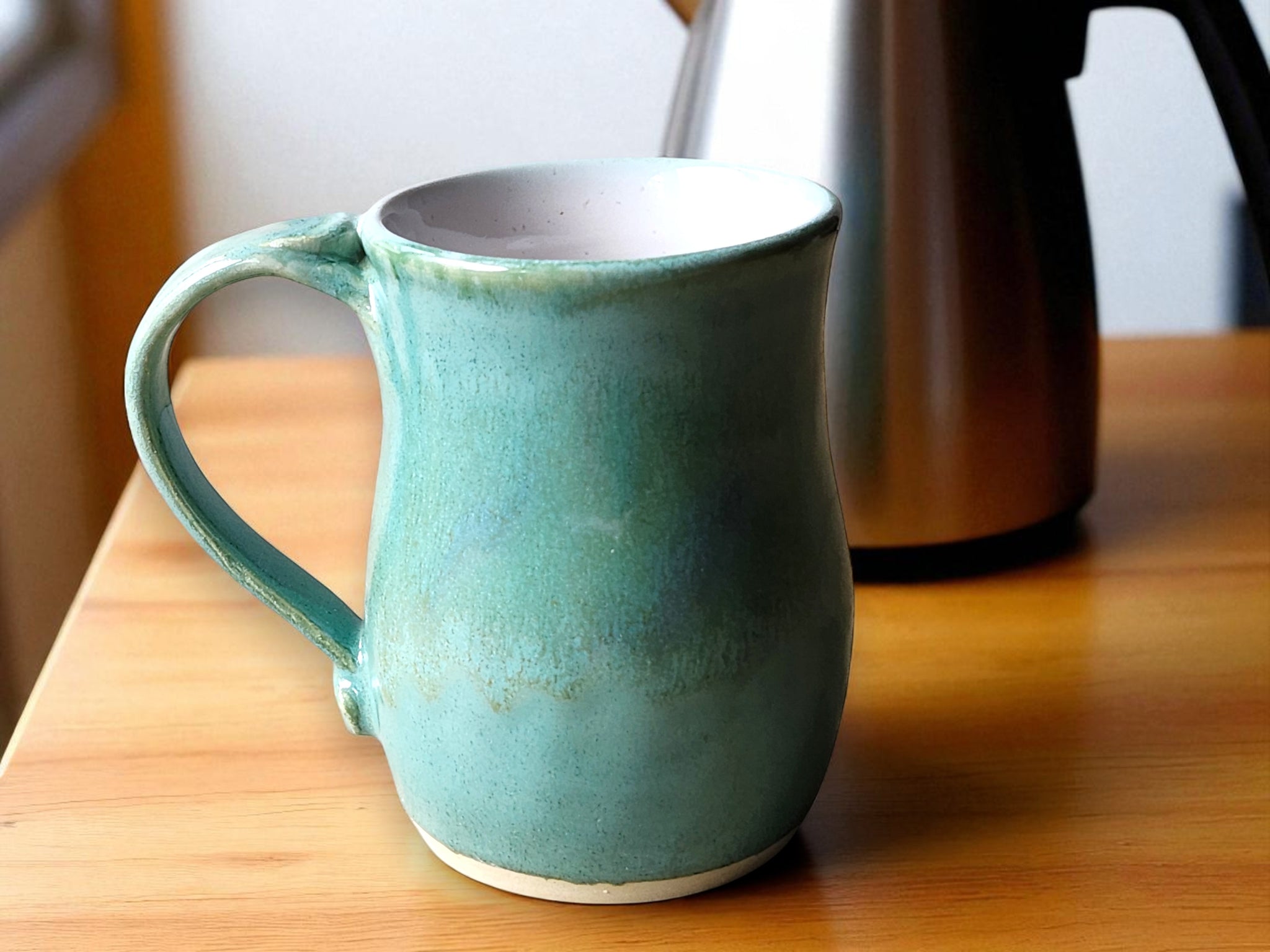 Handmade stoneware mug with mottled green exterior and white interior