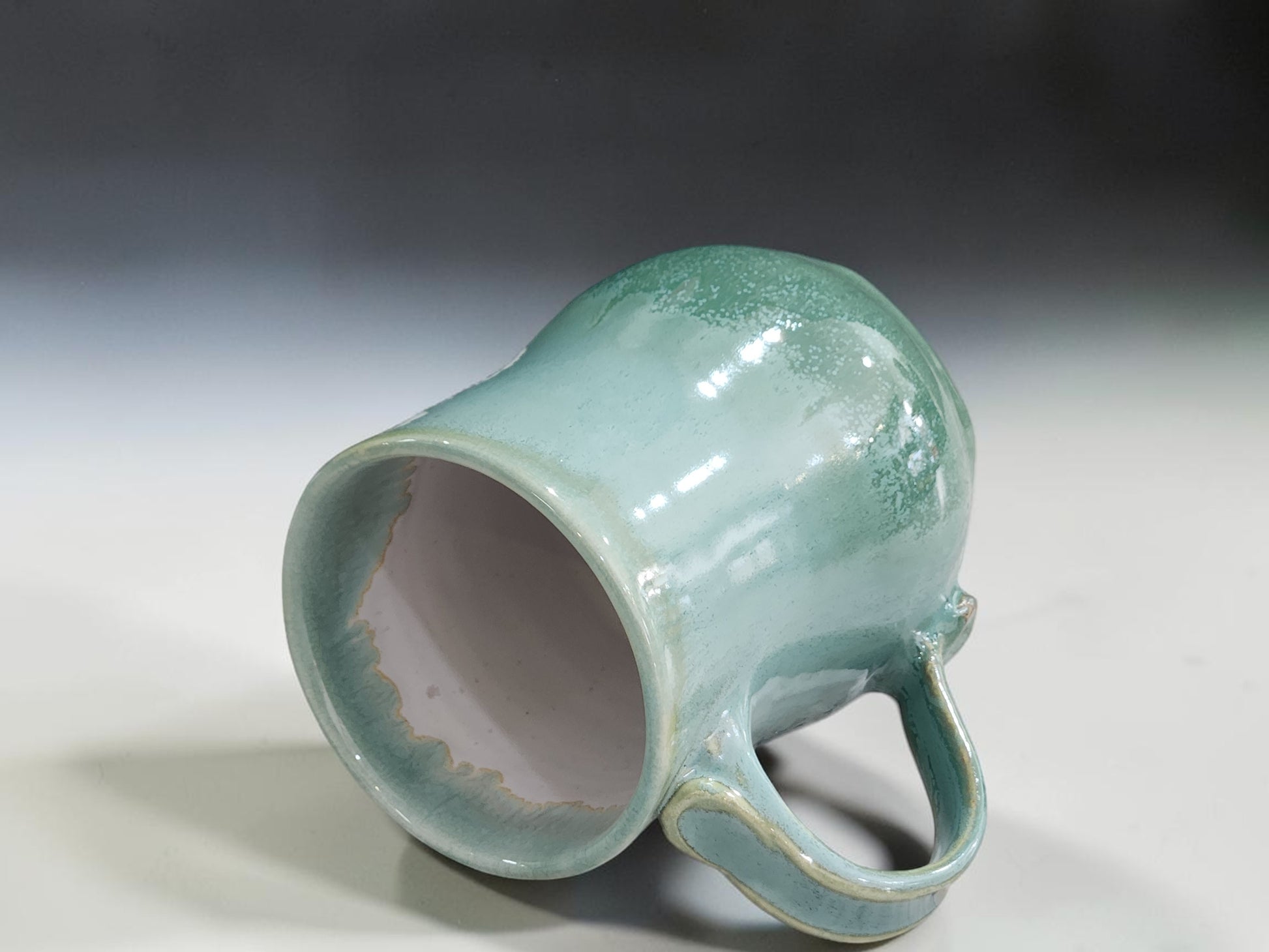 Handmade spearmint green pottery mug laying on its side showing the lining glaze.