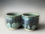 Handmade pottery yunomi with a  glossy green glaze over lapped with a blue black runny glaze.