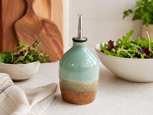 Handmade ceramic oil bottle in spearmint, oatmeal and terracotta glaze styled in a kitchen with salad bowls