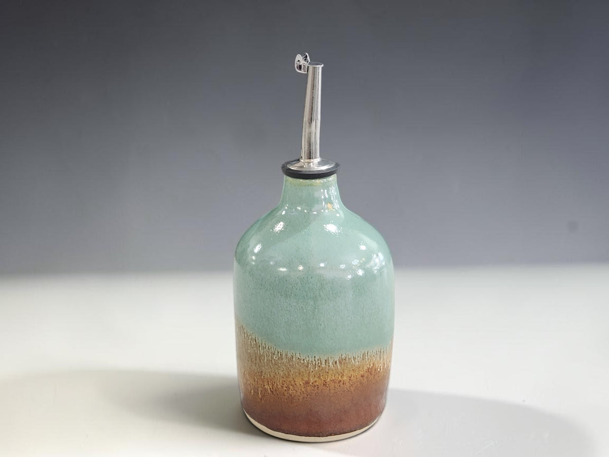 a tall ceramic oil bottle in a mint green and tonal brown glaze made in Australia.