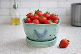 Green ceramic berry bowl with mottled blue glaze and draining holes