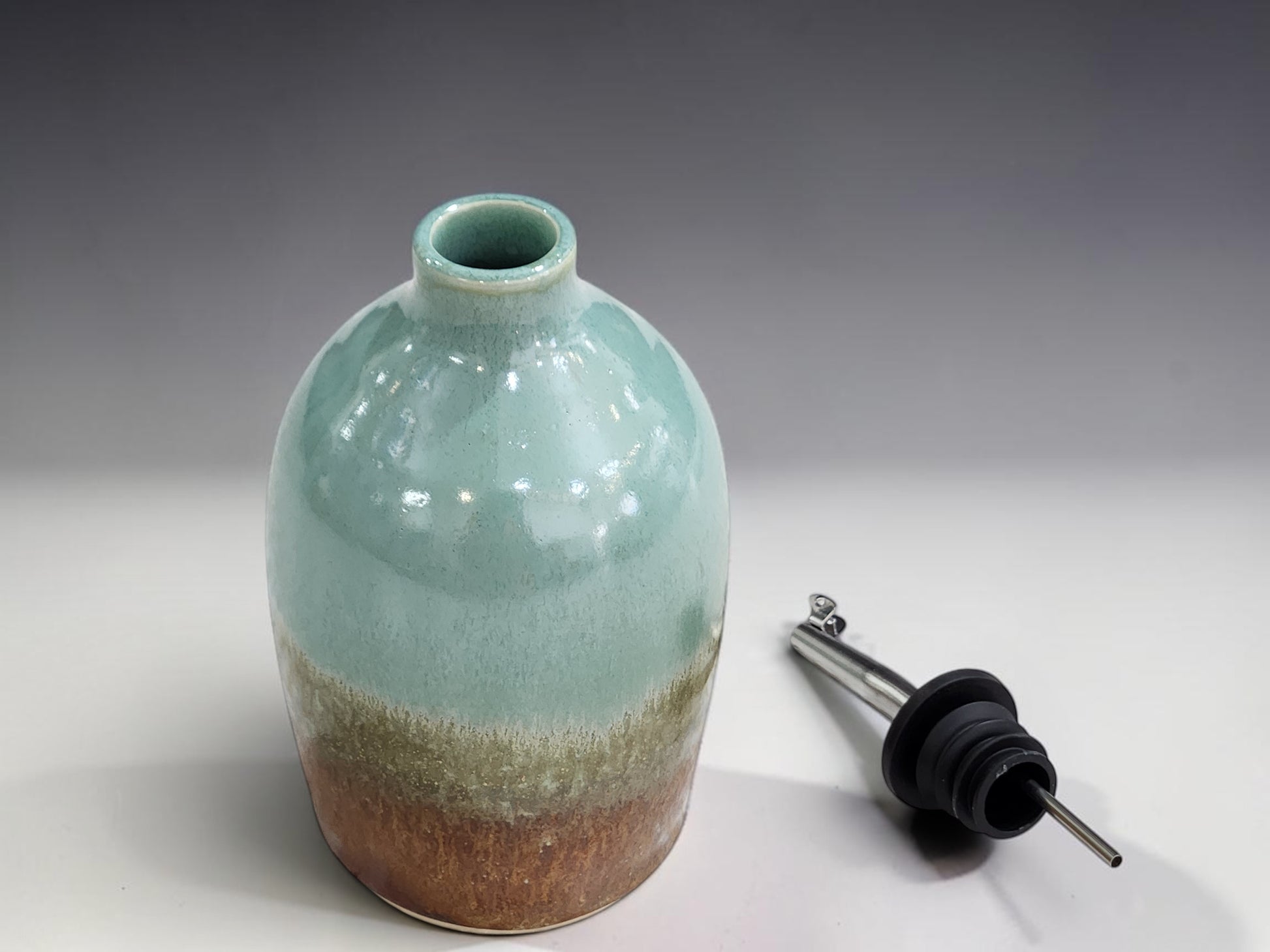 Handmade pottery oil dispenser with soft green glaze and warm brown base, ideal for olive oil or vinegar