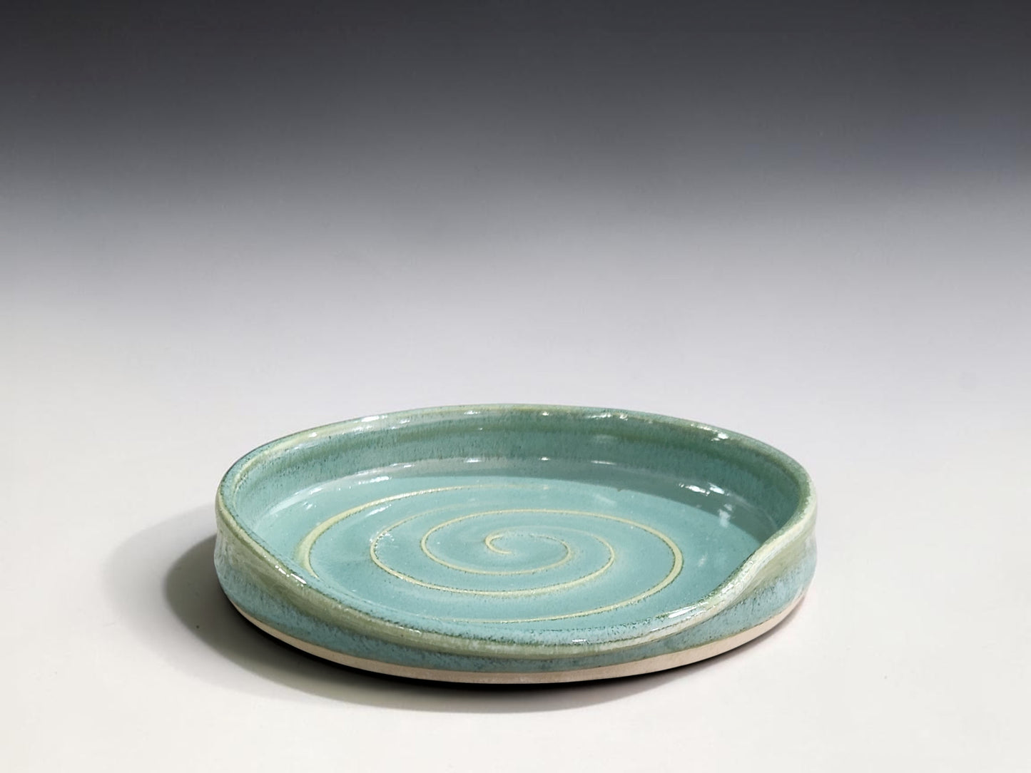 Spearmint green handmade pottery spoon rest with spiral design for resting cooking spoons and kitchen utensils.