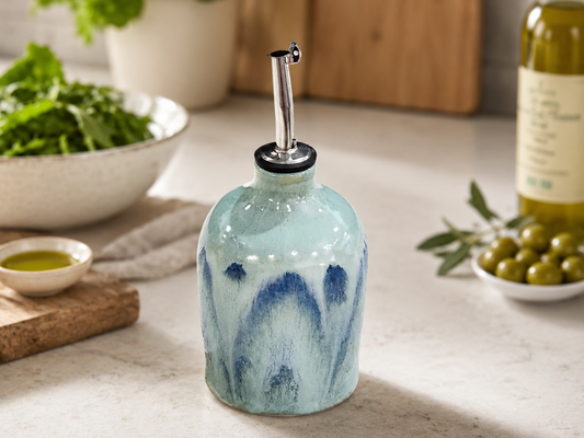 Handmade ceramic oil bottle in soft blue green glaze styled in a kitchen with salad and olive oil