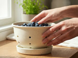 Speckled cream berry bowl with saucer to catch water drips with blue berries shown in it. 