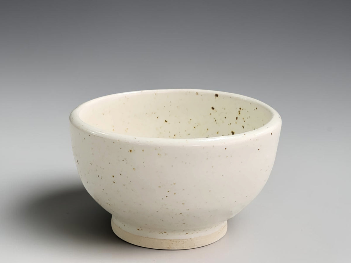Handmade speckled cream ceramic bowl by Buxton Pottery with rounded sides and a raised foot.