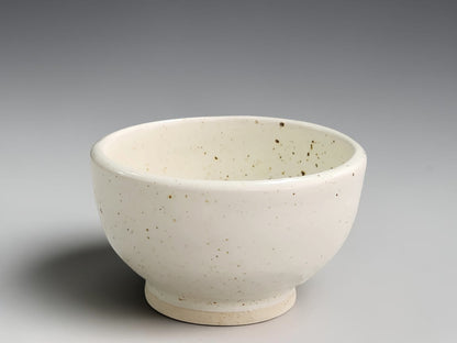 Handmade speckled cream ceramic bowl by Buxton Pottery with rounded sides and a raised foot.