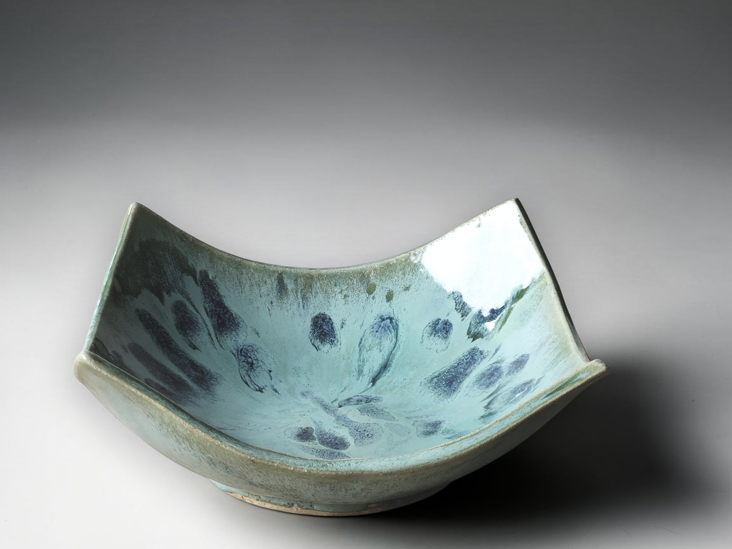 Handmade ceramic serving bowl with blue speckled glaze and sculptural curved edges