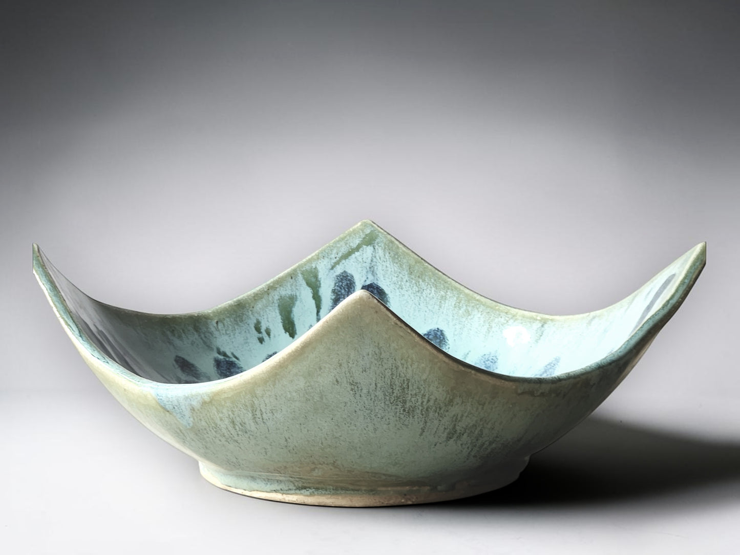 Artisan stoneware bowl with abstract blue floral glaze detail and elevated corners